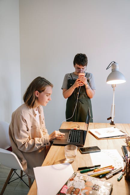 Zwei junge Frauen bei der Telekommunikation – eine arbeitet am Laptop, die andere nutzt ein Smartphone, beide in einem modernen Homeoffice-Setting.